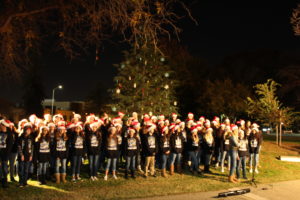 Photo of the Christmas Tree Lighting Ceremony from 2017 showing the decorated tree and a choir of school children wearing santa hats