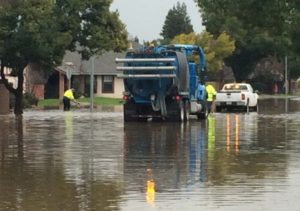 photo shows flooded road with utility workers trying to fix the issue.