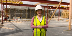 Woman, Amy Hance, in hard hat and safety vest, stands in middle of construction site