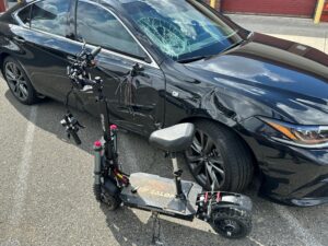 Electric scooter and car involved in collision, both showing damage.